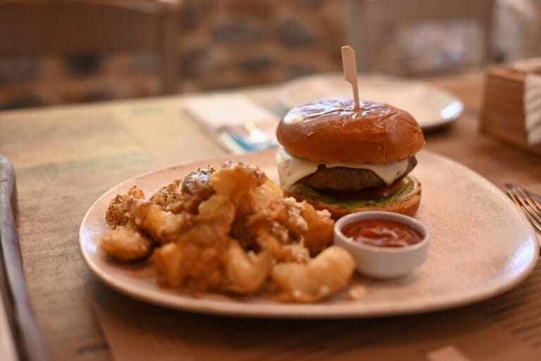 Ένα πιάτο με ένα burger και τηγανητές πατάτες, συνοδευόμενο από σάλτσα.